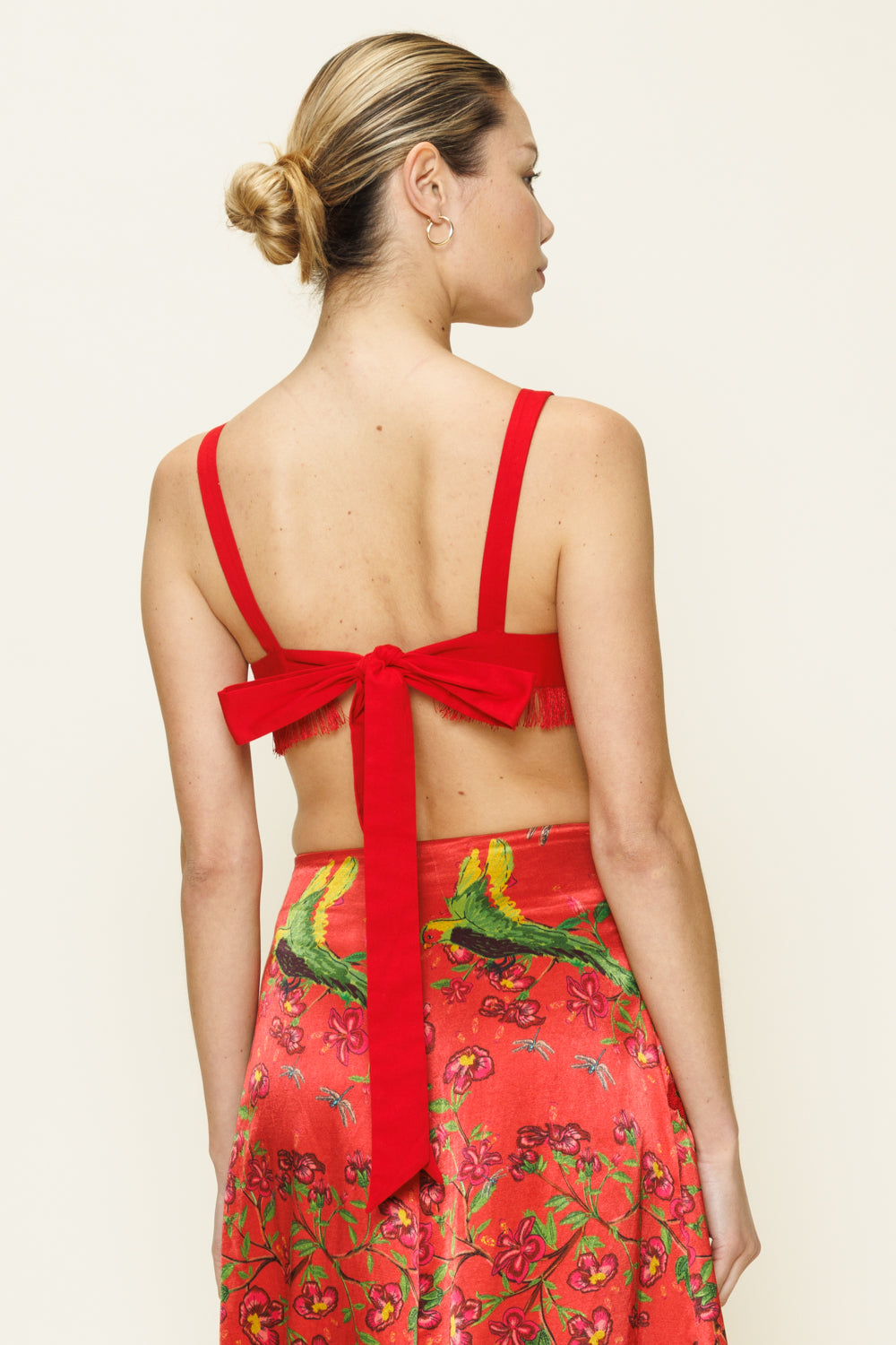Woman wearing a red skirt with a floral pattern and a top with a large bow on the back against a beige background