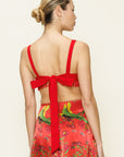 Woman wearing a red skirt with a floral pattern and a top with a large bow on the back against a beige background