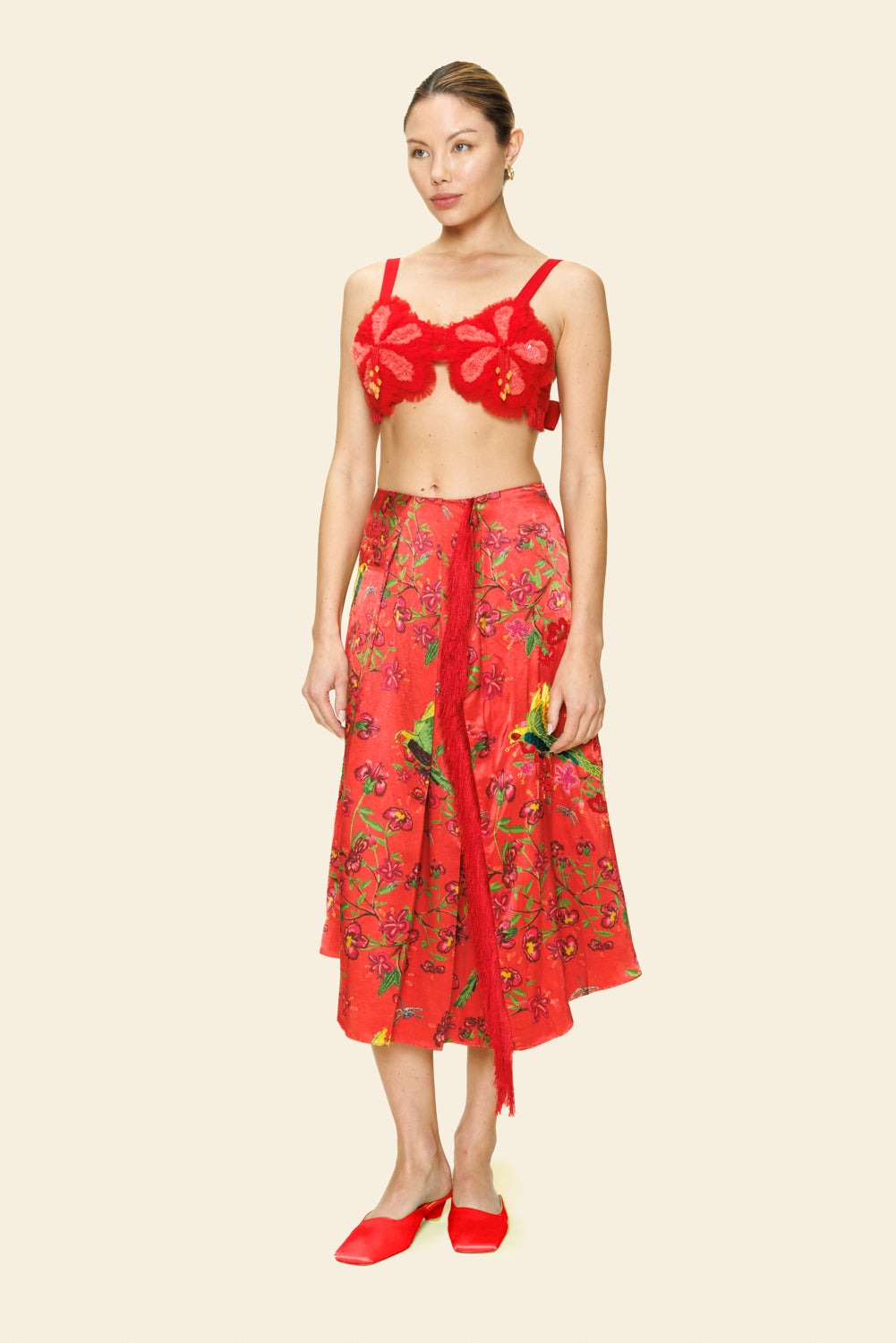 Woman wearing a red floral skirt and bra top outfit on a beige background