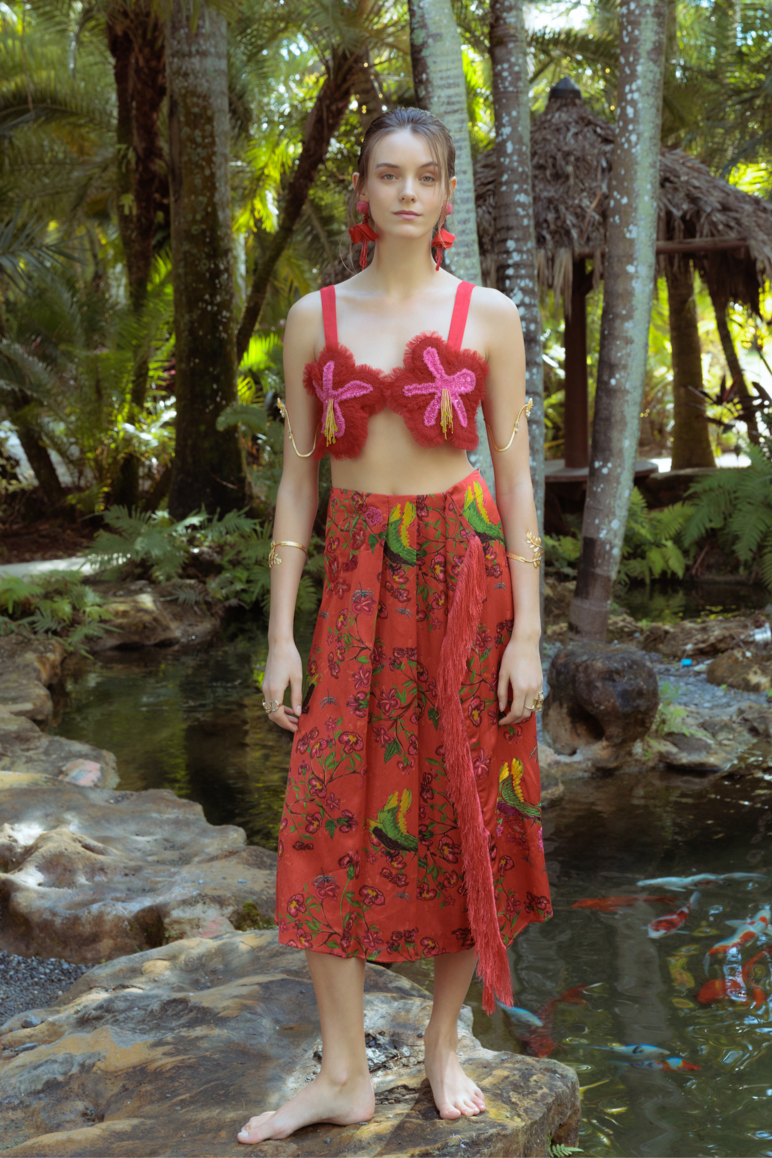 Woman in a red outfit standing in a tropical setting with palm trees and a pond.