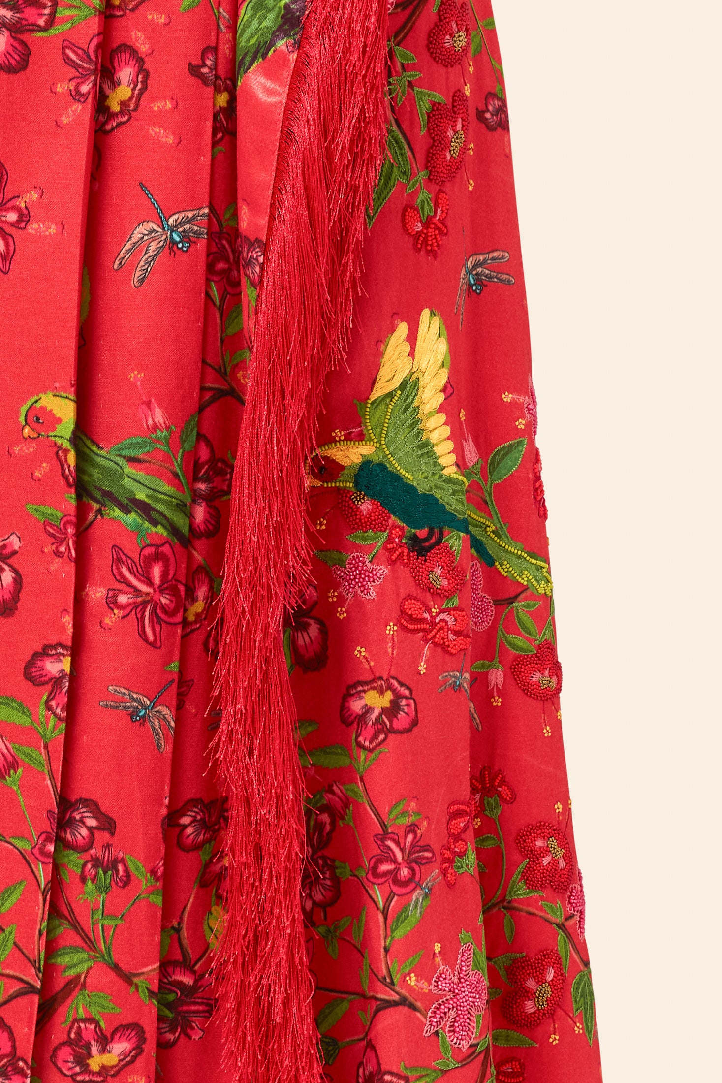 Red fabric with green and yellow bird pattern and red fringe