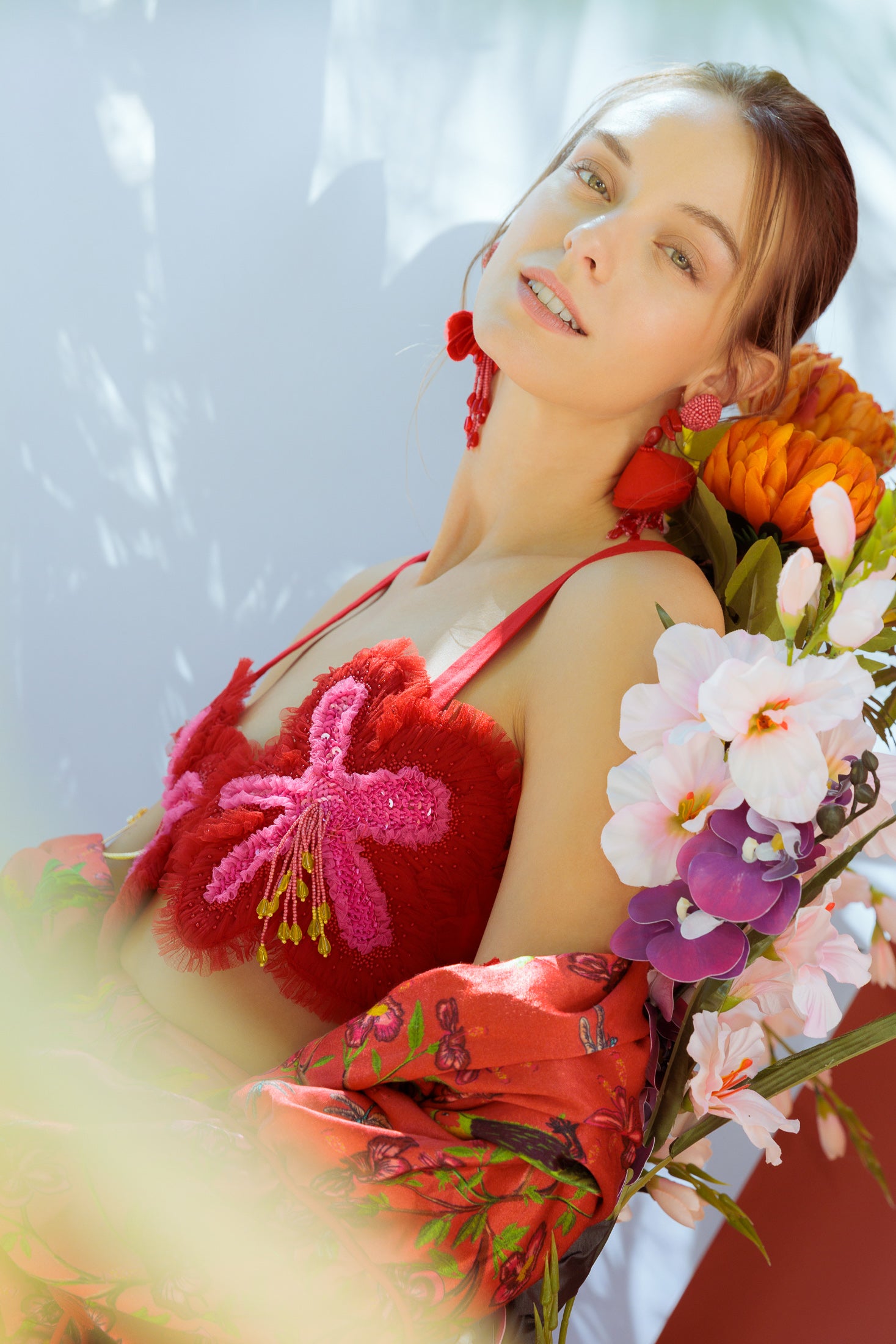 Woman wearing an embroidered bra top surrounded by flowers against a light background