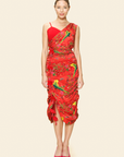 A model wearing a red one-shoulder draped midi dress with a floral pattern and beaded detail on the asymmetrical hem.