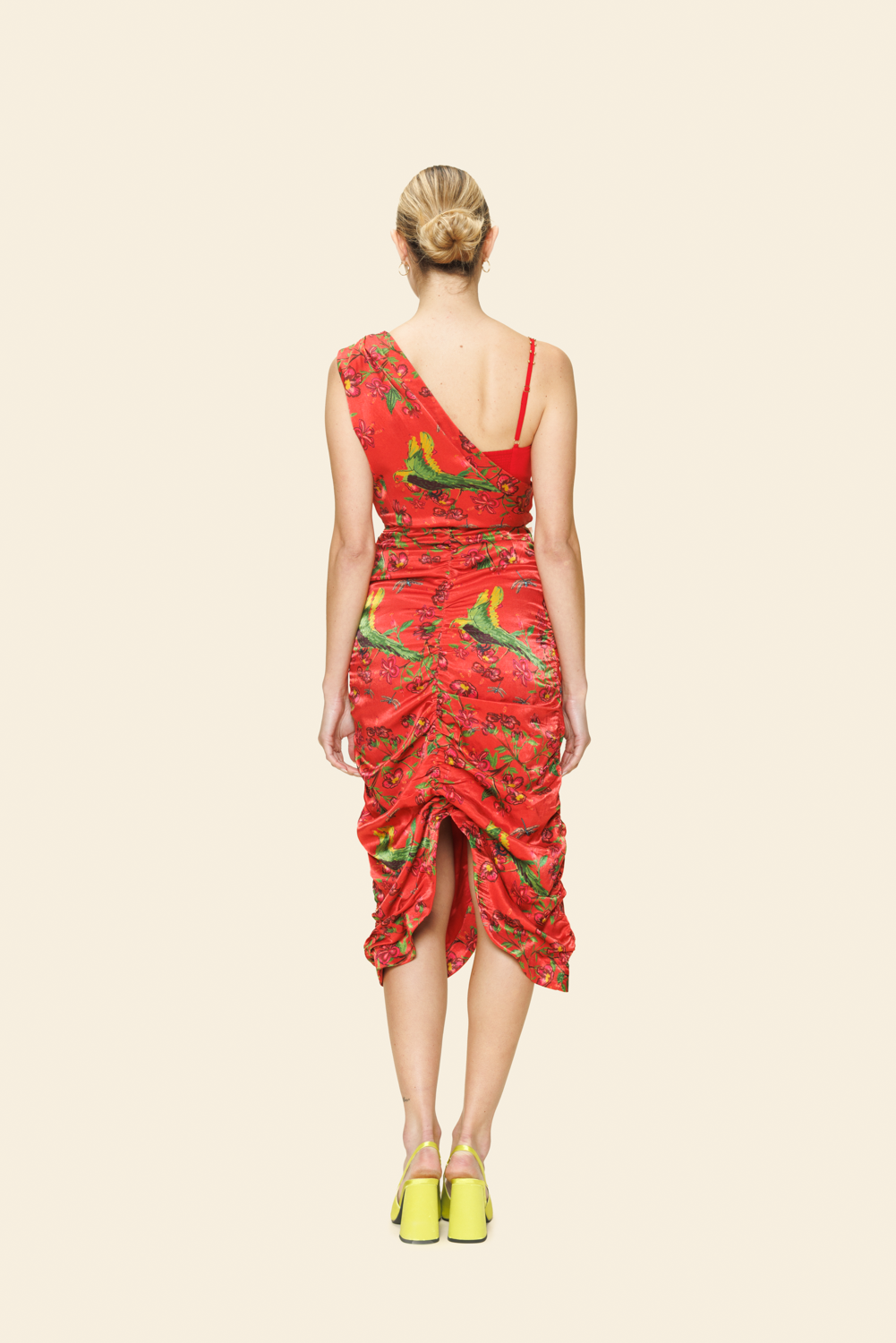 Model wearing a red dress with bird pattern on a beige background seen from the back