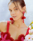 Woman wearing a top with floral details and red earrings, holding flowers against a light background 