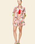Woman wearing a colorful outfit with a red top, embroidered shorts and green shoes on a beige background