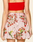Person wearing a red crop top and floral shorts with birds on a beige background