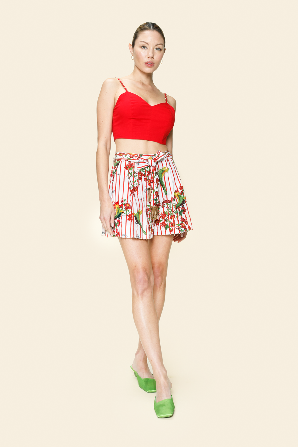 Woman wearing a red top and floral  and bird printed shorts on a beige background