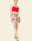 Woman wearing a red top and floral  and bird printed shorts on a beige background