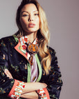 Woman wearing a colorful embroidered jacket with a neutral background