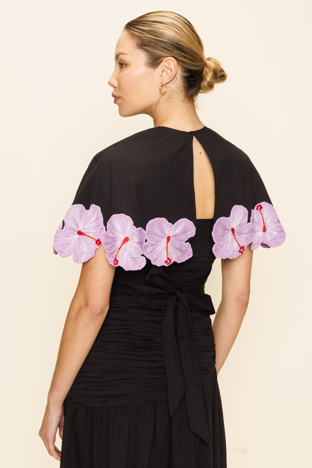Woman wearing a black cape with pink floral appliqué seen from the back
