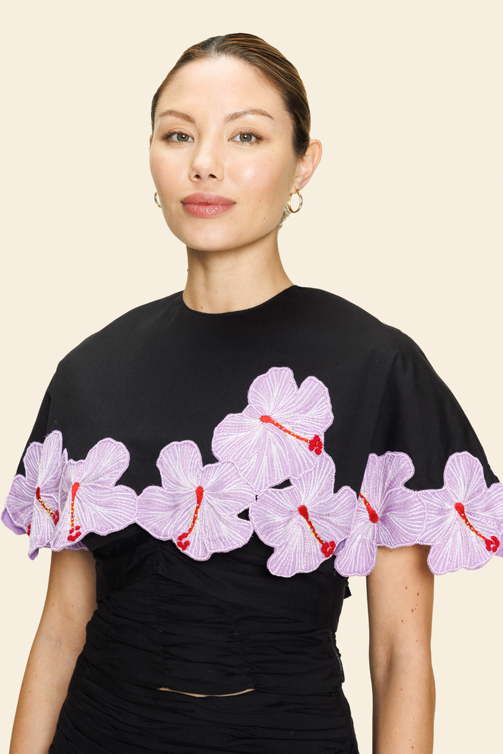 Woman wearing a black cape with pink floral appliqué 