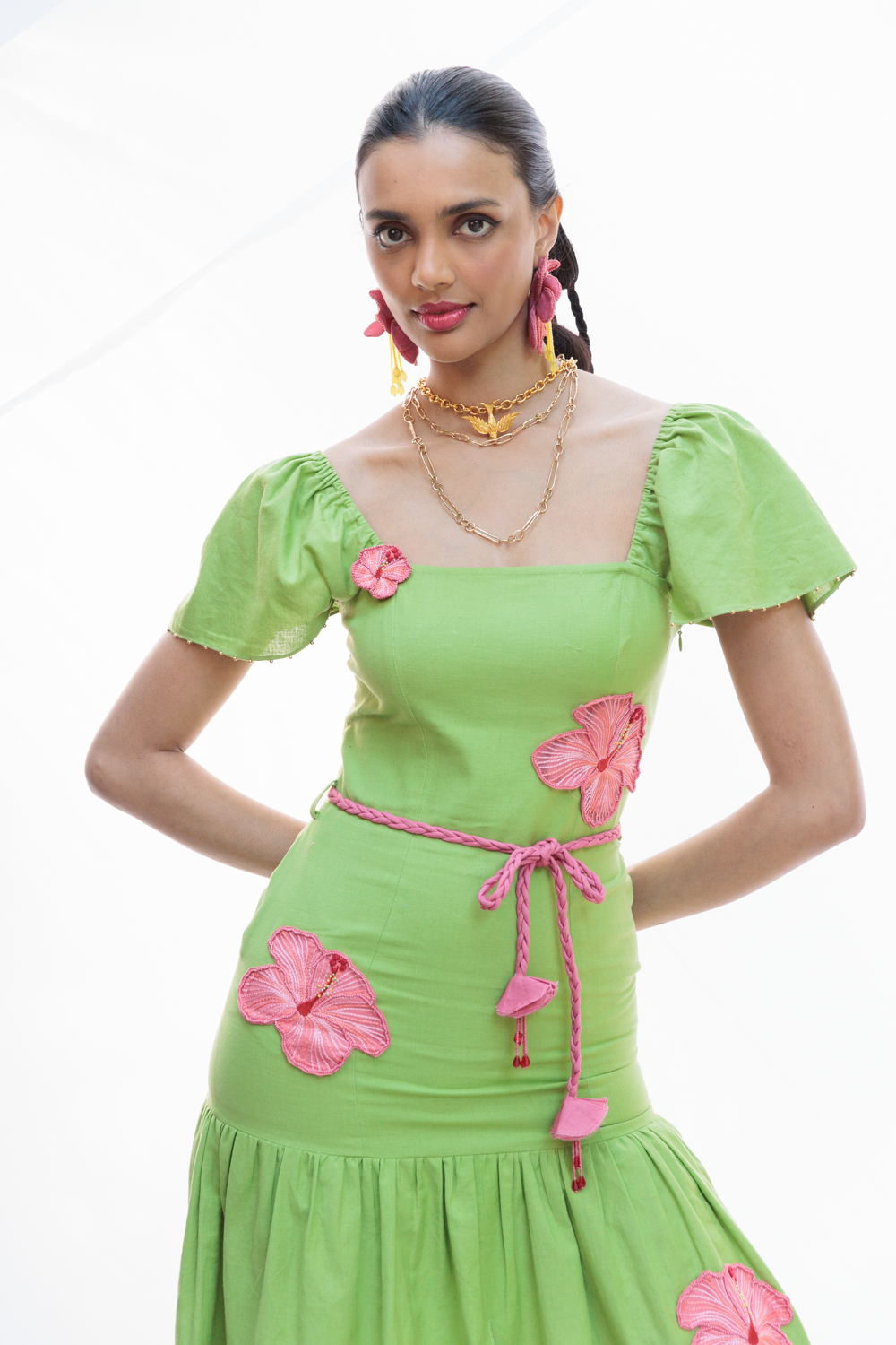 Woman wearing a green dress with pink floral embellishments on a white background