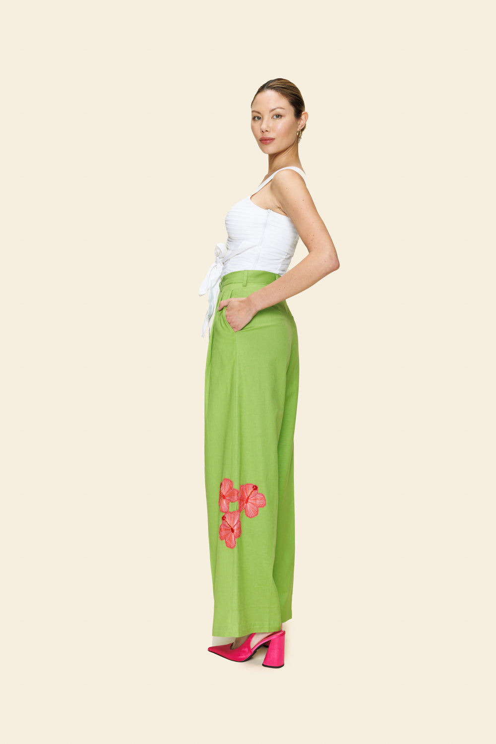 Woman wearing a white top and green pants with pink floral details on a beige background