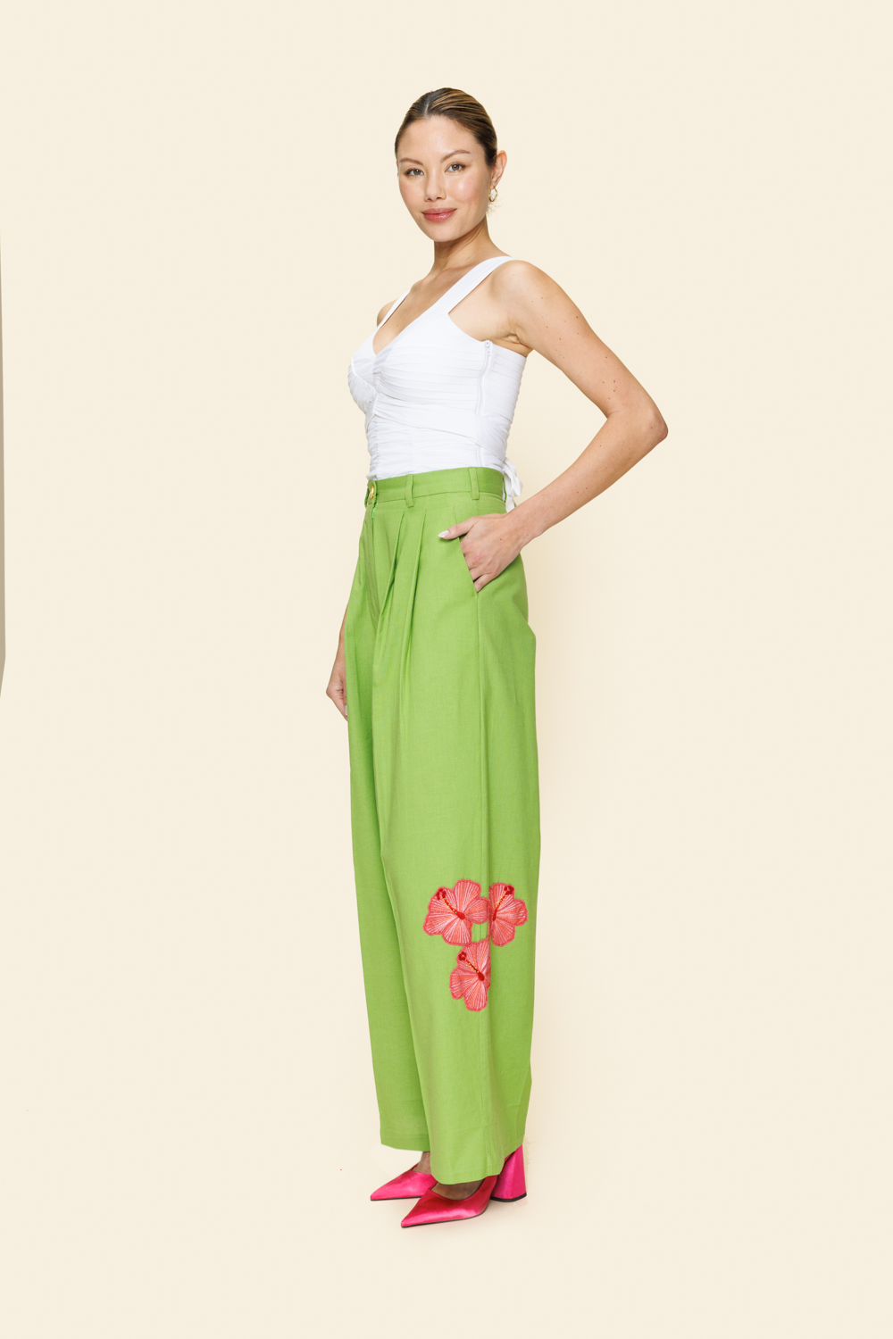Woman wearing green pants with floral embellishments on a plain background