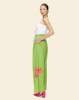 Woman wearing a white top and green pants with pink floral details on a beige background