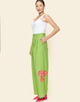 Woman wearing green pants with floral embellishments on a plain background