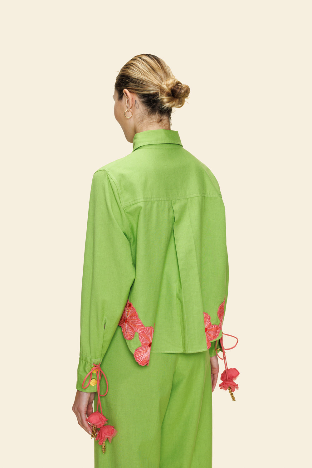 Person wearing a green outfit with pink floral details on a beige background
