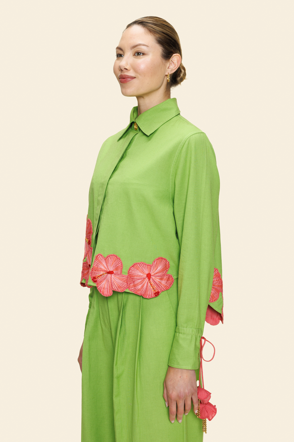 Woman wearing a green shirt and pants with pink floral accents on a beige background