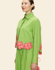 Woman wearing a green shirt and pants with pink floral accents on a beige background