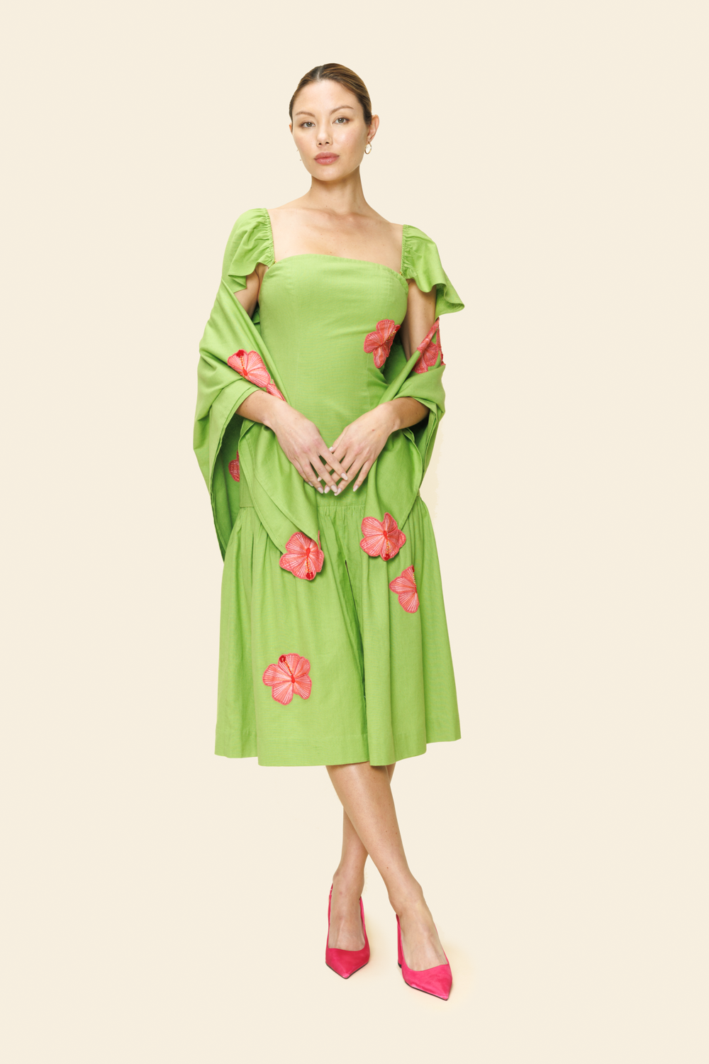 Woman wearing a green dress and shawl with pink floral details on a beige background