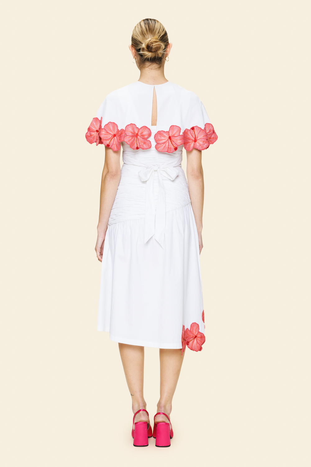Woman wearing white skirt and cape with pink floral details on a beige background