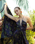 Woman in a floral dress holding a patterned fabric against a natural background