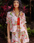 A woman wearing a colorful floral outfit with florals in the background