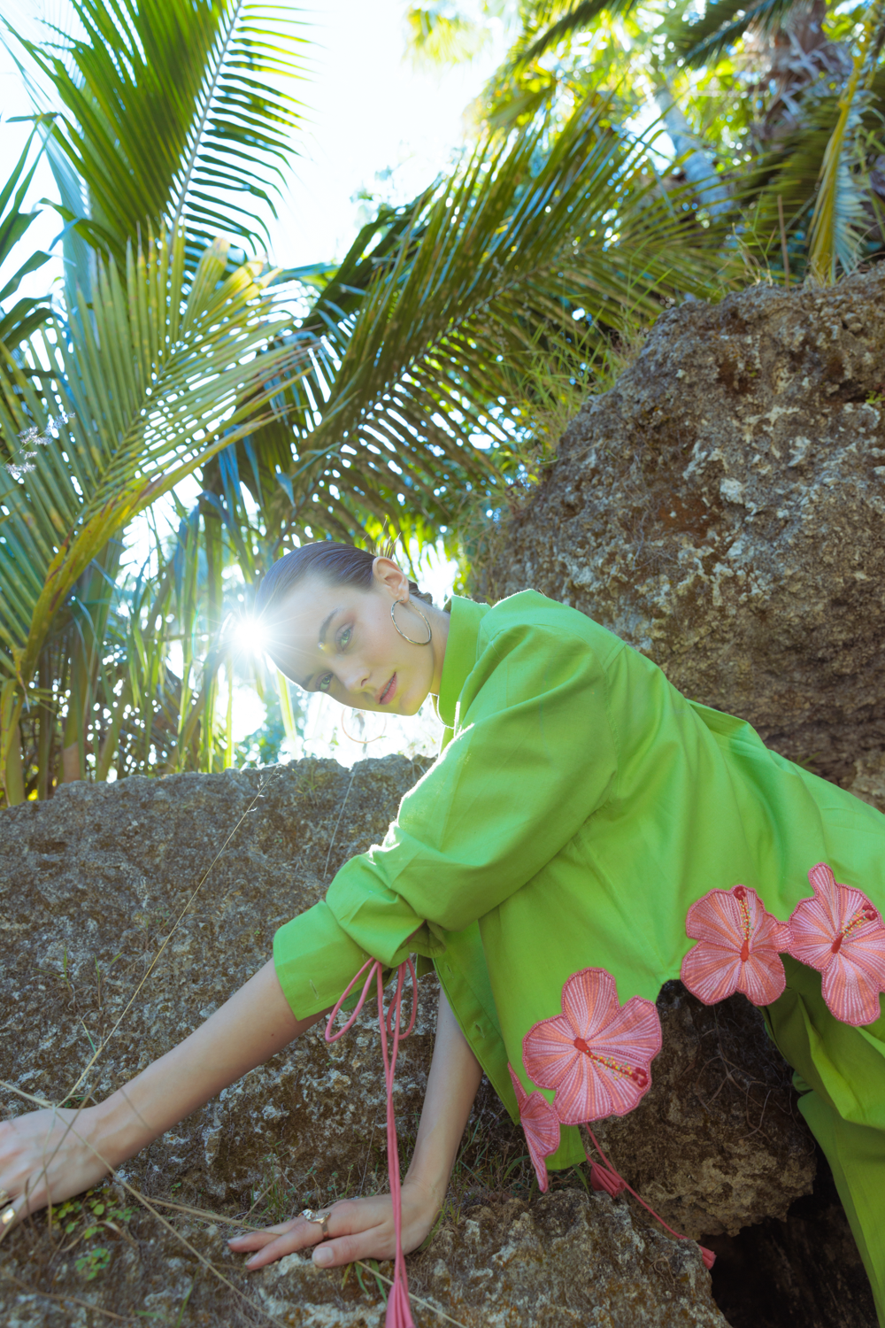 Person in a green dress with pink floral patterns sitting on rocks in a tropical setting