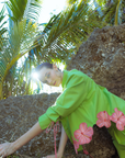 Person in a green dress with pink floral patterns sitting on rocks in a tropical setting