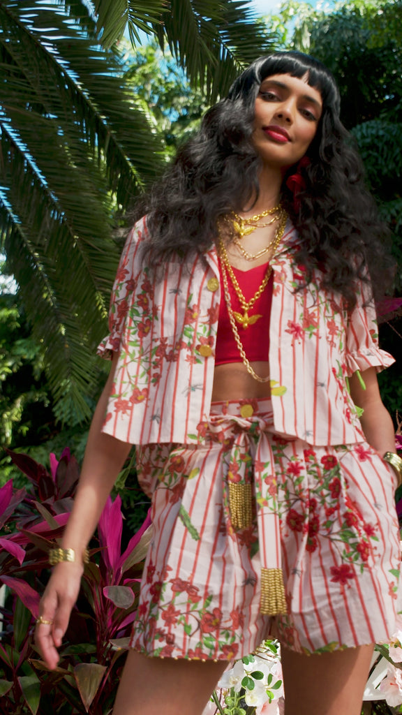 video of woman wearing red striped floral shirt and short, surrounded by palmtrees and florals