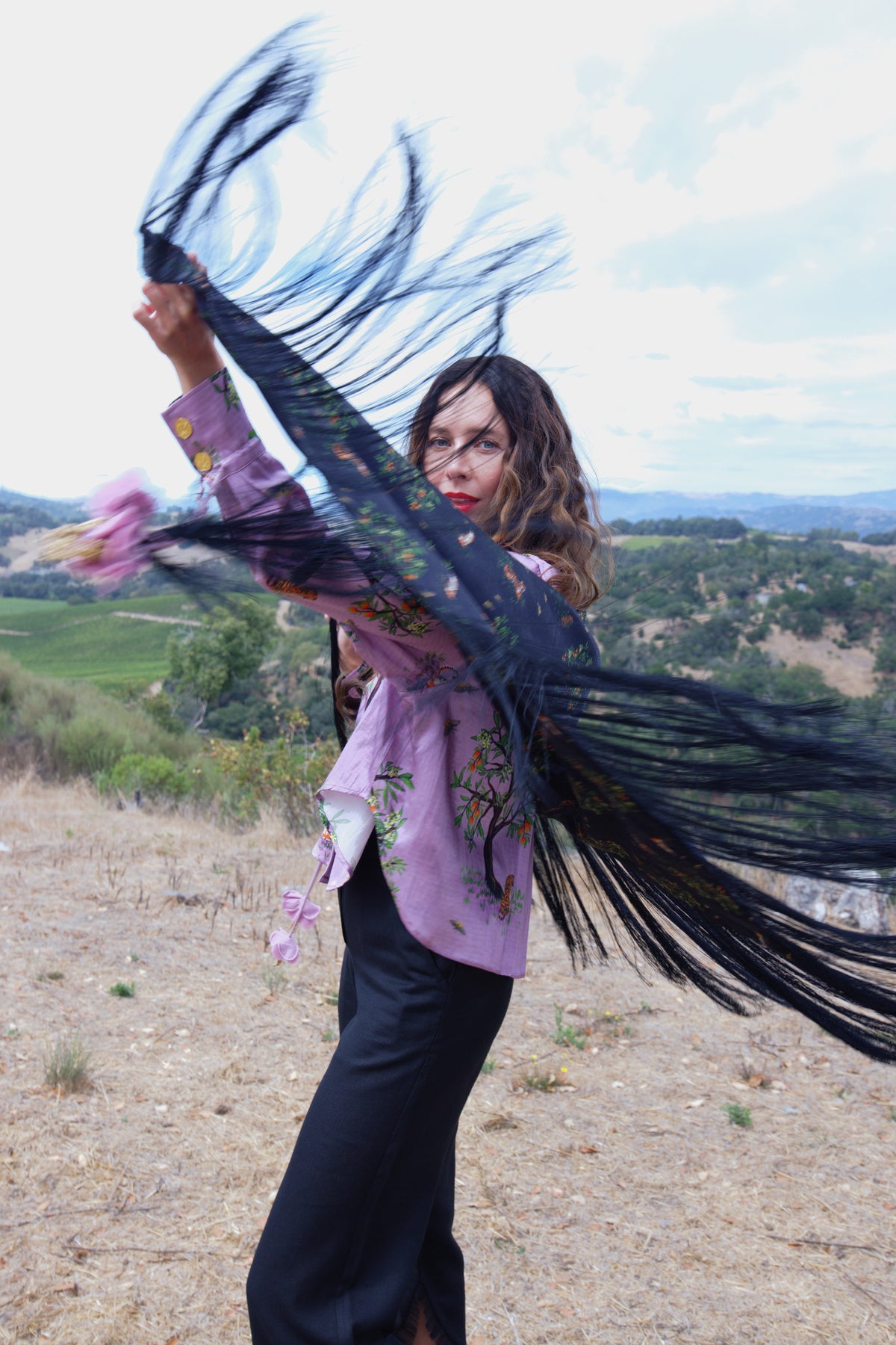 Ashaki model in a lilac printed shirt lifting a fringed shawl in the open air